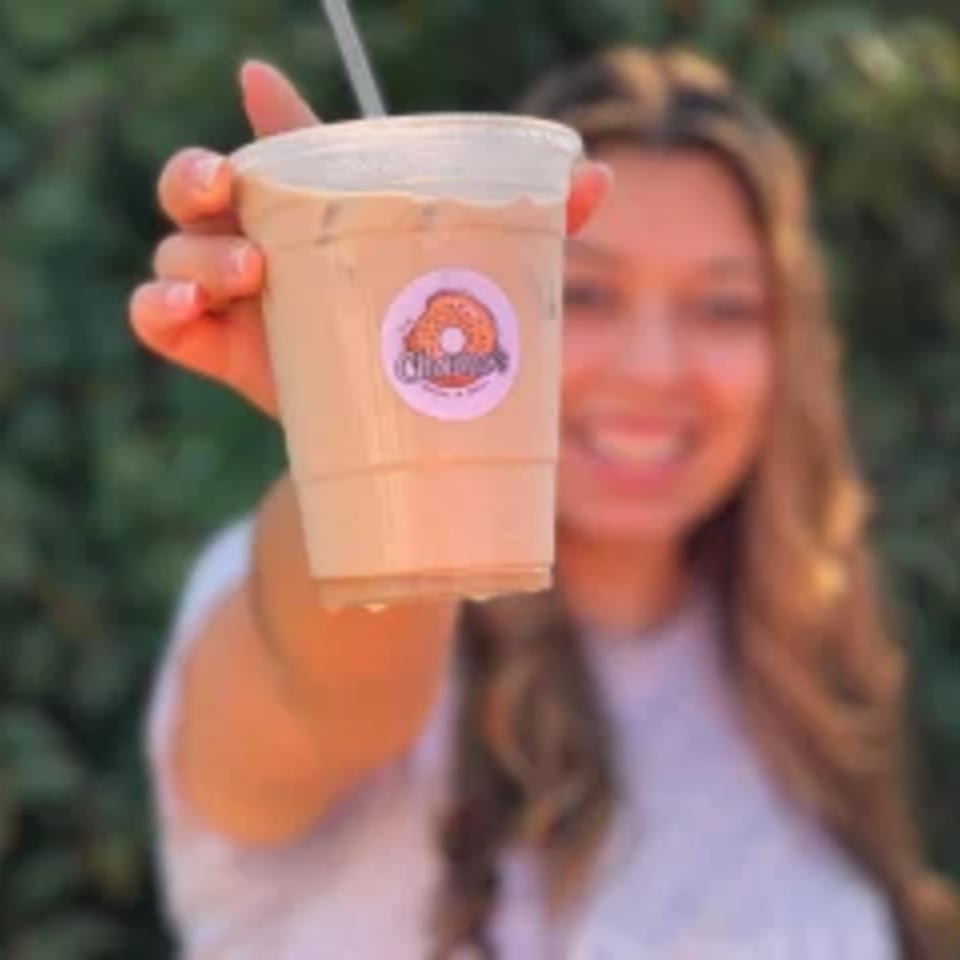A smiling woman holds up an iced coffee with a Chamo's Bagel & Grill logo sticker.
