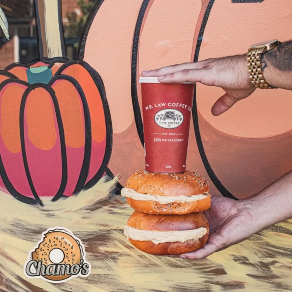 A hand holds two Chamo's bagels with cream cheese, topped with a red coffee cup.
