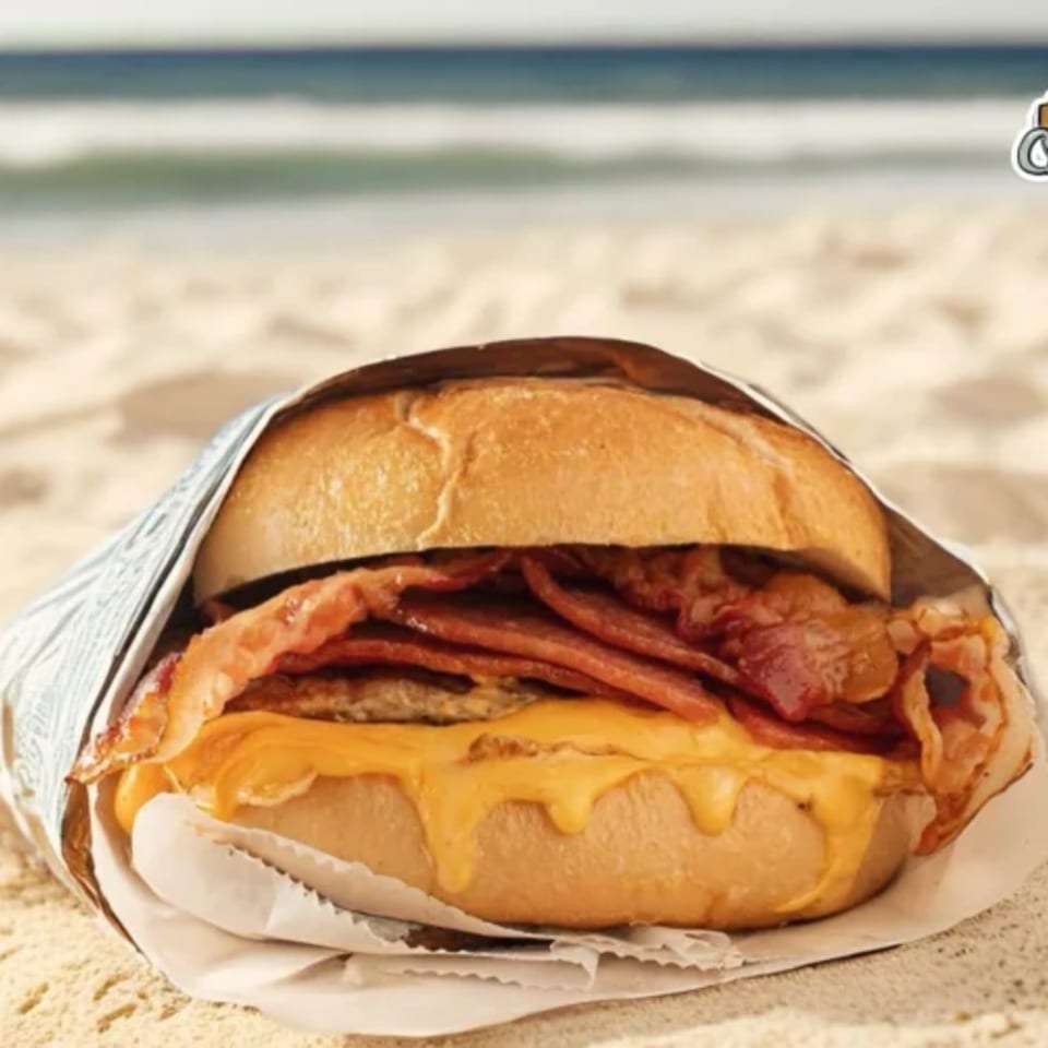 Chamo's Bagel & Grill bacon, egg, and cheese bagel on a beach with ocean in background.